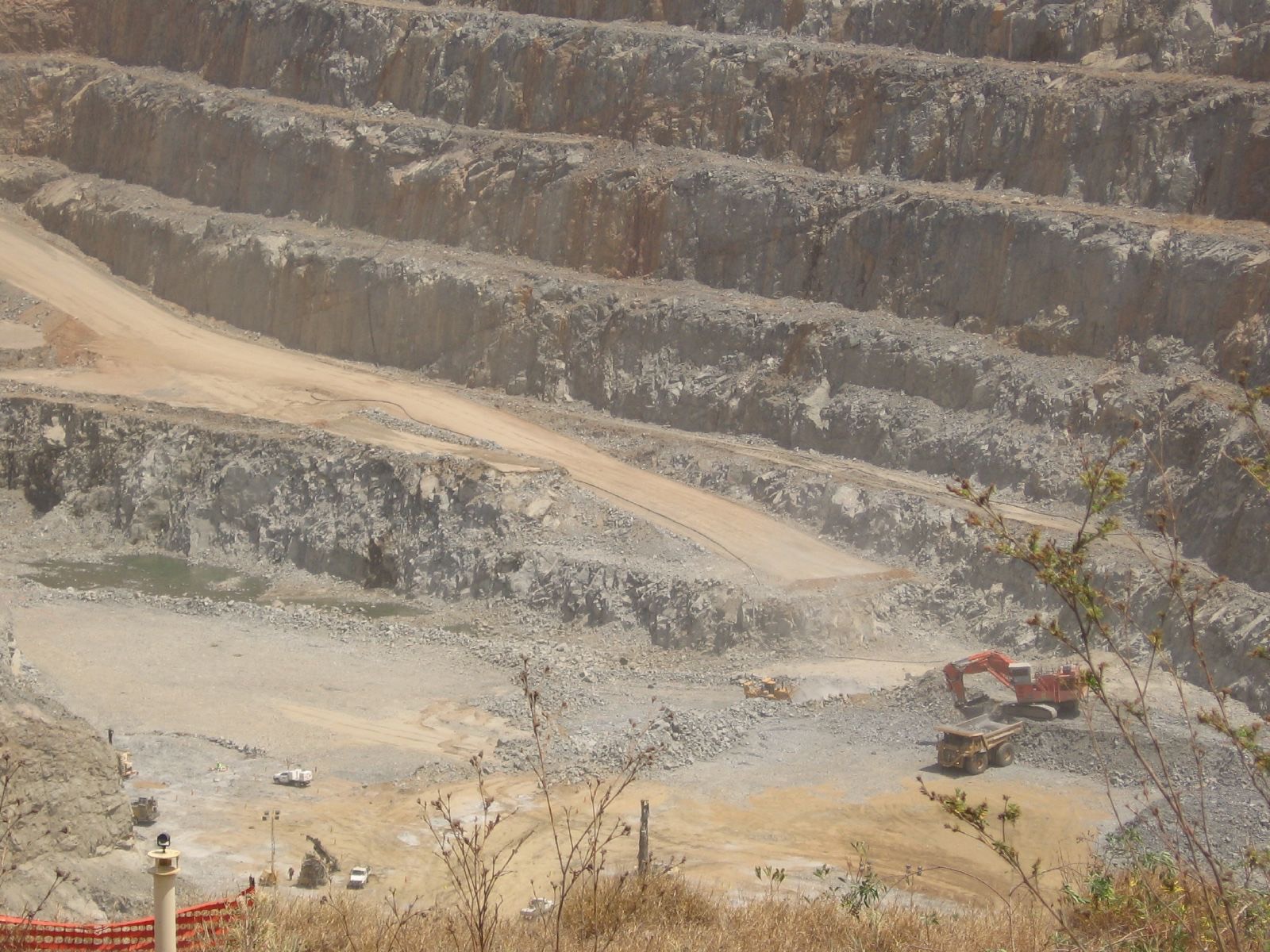 Excavator loading a haul truck on the floor of a terraced open-pit mine